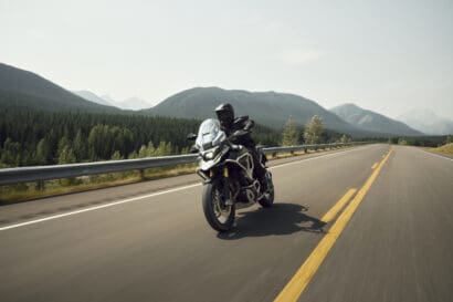 A motorcyclist riding a Triumph Tiger 1200 adventure bike along a mountain highway.