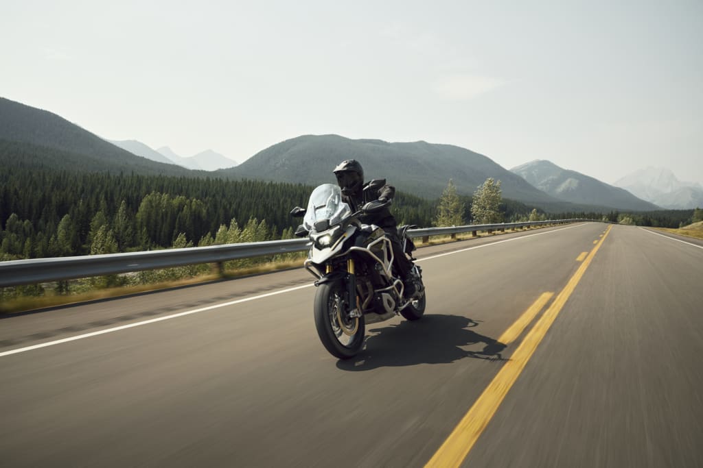 A motorcyclist riding a Triumph Tiger 1200 adventure bike along a mountain highway.