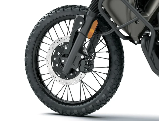 Close-up of a Kawasaki KLR650 front wheel with a spoked rim, knobby tire, and disc brake assembly.