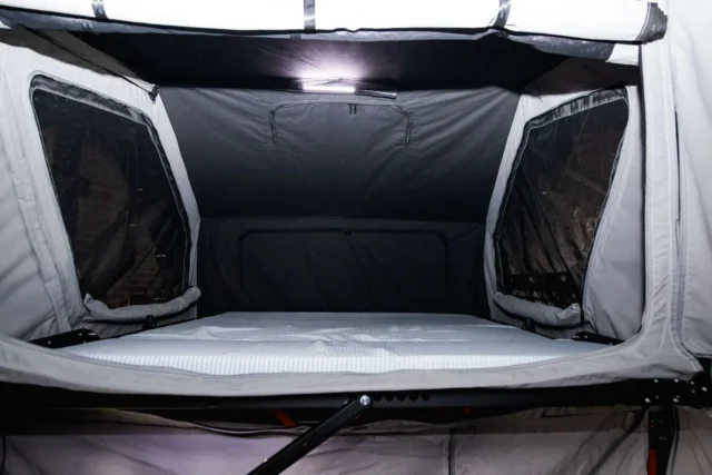 Interior view of a Patriot Campers rooftop tent featuring a mattress, mesh-screened side windows, and an overhead LED light.