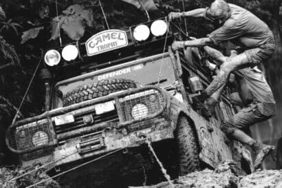 two men clinging to the outside of a muddy SUV